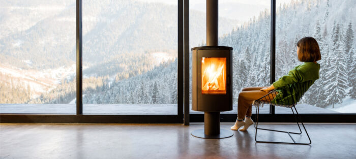 warmth- A woman enjoying the view of Of a snowy landscape while sitting inside by the fire